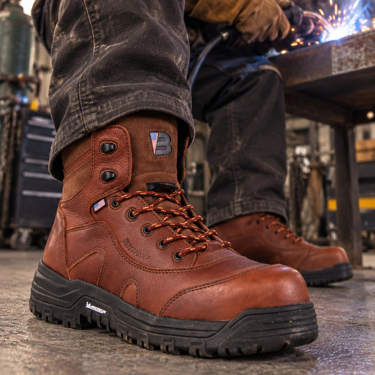Welder wearing copper-brown US Boot Iron Master boots with black Michelin soles in a metal fabrication workshop.