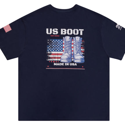 A navy blue short-sleeve t-shirt with a patriotic graphic on the front featuring the text 'US BOOT EST.2025' above a distressed American flag and a pair of combat boots, with 'MADE IN USA' below.