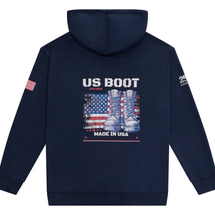 A navy blue hooded sweatshirt shown from the back, featuring a large graphic print of combat boots over an American flag with the text 'US BOOT' and 'MADE IN USA'. A small American flag graphic is on the right sleeve, and a white graphic is on the left sleeve.